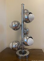 Front and side view of the chrome eyeball lamp showing six spherical light fixtures attached to a central pole with a round base.