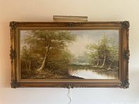 Full view of framed horizontal oil painting depicting trees and a river, hung on a wall.