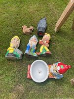 Photo showing four garden gnomes, one squirrel figurine, and one plastic owl on grass