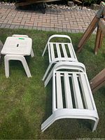 Four white garden stools shown stacked and placed on grass outdoors, three matching with slatted tops and one smaller flat-seated stool.