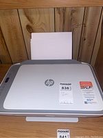 Front view of HP Deskjet 2755e printer showing loaded paper on input tray and MaxSold sticker on top.