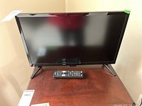 Front view of the 21 inch Insignia flat screen TV with remote placed on stand.