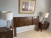 Pair of lamps on wooden nightstands with wood headboard and flower painting