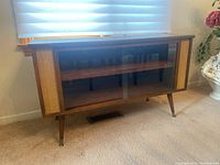Frontal view of the wood veneer Mid-Century Modern cabinet showing sliding glass doors and decorative end panels.