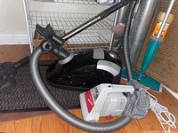 Photo showing Miele canister vacuum with hose, metal extension wand, and floor attachments alongside Kenmore handheld vacuum on floor.