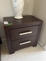 Photo showing a dark brown nightstand with two drawers and silver metal handles, visible scratches on top surface.