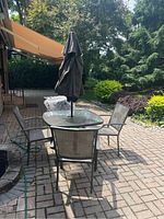 Outdoor patio set with table, umbrella, and four chairs shown on brick patio.