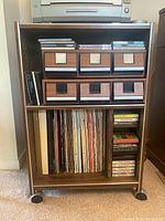 Front view of wood veneer music cabinet showing drawers, vinyl records, CDs, and cassettes.