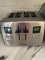 Front view of the stainless steel four slice toaster showing dual control panels with digital displays, sliders, and function buttons.