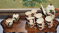 Photo showing 13 stacked tea cups, creamer, and sugar bowl with apple motif on a wooden table.