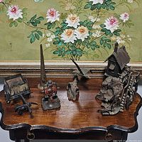 Five antique metal art pieces arranged on wood surface with floral painting background