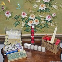 Photo showing various candles including tea lights in plastic bag, blue and beige tea lights in box packaging, red votives in plastic and white small candles along with cream tapered candles and a box of red tapers.