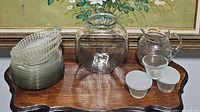 Photo of all glassware items together on a wooden table, showing plates stacked, clear pitcher, small containers, and crystal dishes