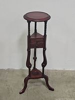 Front view of dark stained wooden pedestal table with round top, barley twist supports, triangular midsection drawer and curved tripod legs.
