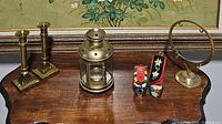 Photo showing entire lot on wooden table, includes 2 brass candlesticks, brass lantern with star cutouts, 2 small colorful decorative boots, and a brass round gong with handle.