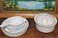 Top view of combined CorningWare dishes, showing blue floral pattern bowls and ceramic spoon on stacked white ribbed casserole dishes with clear lids.