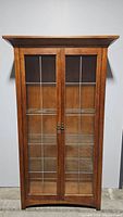 Front view of the closed curio cabinet showing wood frame and glass doors with grid pattern.