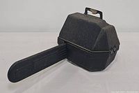Chainsaw stored in black hard plastic carrying case, side view showing the closed case and part of the chainsaw bar
