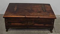 Closed view of the wooden blanket chest showing dark stained top with metal hinges and latch.