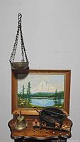 Full view of the hanging incense burner in front of framed landscape painting, along with bell, iron pot, and key hook on wooden table.