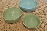 Three mixing bowls arranged on a textured surface, showing two green bowls and one light blue bowl from a top angle.
