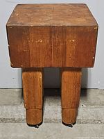 Front view of the petite butcher block table showing the thick wooden top and two solid wooden legs with caster wheels.