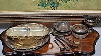 Full view of assorted silver serving trays, small bowls, creamer, and utensils displayed on wood surface.