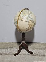 Full view of the globe showing the wooden tripod and part of the globe's surface with world map details.