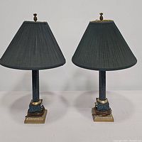 Pair of matching table lamps with dark green shades and marble-look columns standing side by side