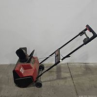 Side view of red and black Toro tiller showing the chute, wheels and handle in a folded position.