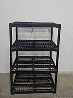 Front view of the black plastic utility shelf showing three grid wire shelves and four sturdy legs.