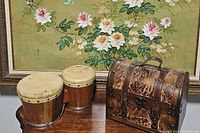 Pair of vintage wooden drums and a vintage treasure chest shown side by side on a wooden surface with floral painting background.