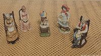 Five vintage porcelain figurines arranged on a surface, showing the set and details of each one.