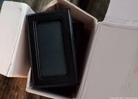 Mini small black digital thermometer device in black plastic casing seen inside the white box packaging.