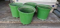 Four green plastic planters shown side by side, outside on concrete floor. Planters are more than 8 inches in height.