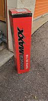 Tall red box with RangeMax branding and shipping label on top, placed outside on pavement.