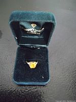 Ring displayed in a dark green velvet jewelry box showing gold band and rectangular topaz stone