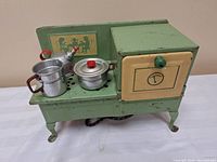 Green metal toy electric stove with cream-colored oven door and green knob, showing paint wear and vintage design.