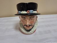 Front view of Royal Doulton Beefeater ceramic character jug showing detailed face and black hat with floral accents.