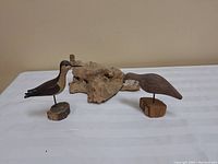 Two carved wooden shore birds mounted on wooden bases with driftwood behind.