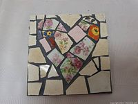 Front view of the mosaic artwork showing heart-shaped assembly of floral patterned crockery pieces and grout background.