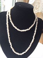 Pearl necklace displayed on black necklace stand showing length and pearl shapes.