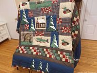 Folded quilt draped over a stand showing cabin, fish and duck appliqués with tree blocks