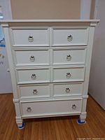 Front view of white highboy dresser with seven drawers and silver ring pulls