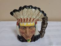 Front view of the Royal Doulton character jug showing the detailed face of the Native American Indian with feathered headdress and carved totem pole handle.