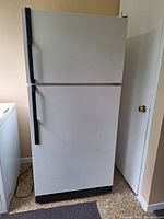 Front view of the white refrigerator with freezer on top closed, showing black vertical handles and base.