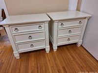 Two white wooden nightstands side by side on hardwood floor