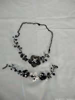Full view of the black wired beaded flower necklace and matching bracelet laid on a white background showing overall design.
