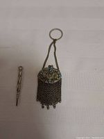Photo of Victorian coin purse and metal pencil on white background, showing size and details of blue stone embellishments and chain fringe on purse.