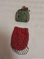 Photo showing rectangular green velvet Victorian purse with metal framed sides and drawstring closure paired with red velvet purse decorated with metal studs and chain fringe.